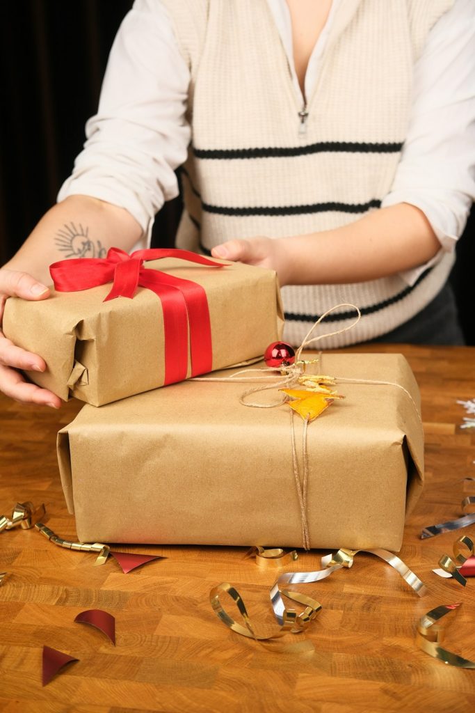 Hands holding small gifts wrapped in brown paper with red ribbon