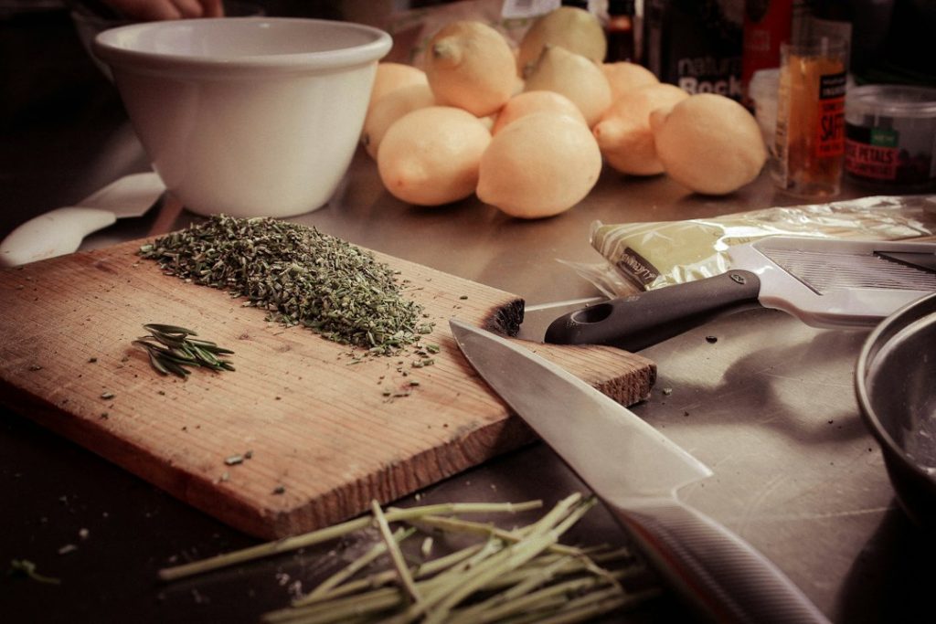 Kitchen counter crowded with a cutting board, chopped herbs, onions and a knife mid-prep