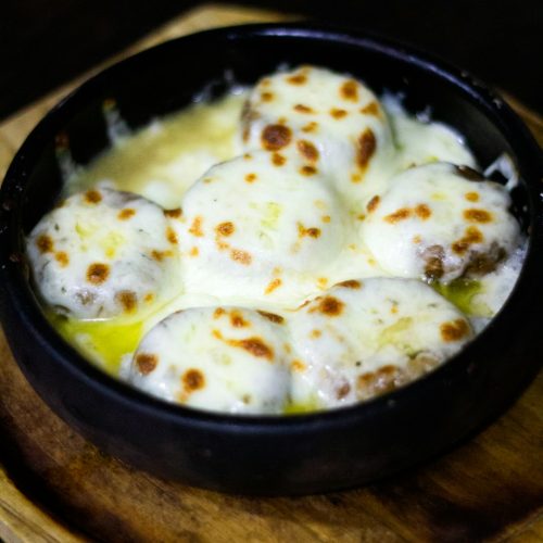 Meatballs baked in a creamy white sauce under golden melted cheese in a cast-iron dish