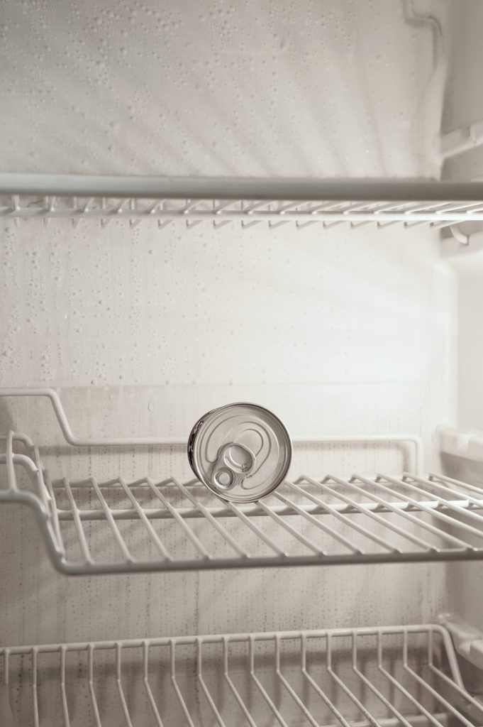 Nearly empty refrigerator shelf with a single can