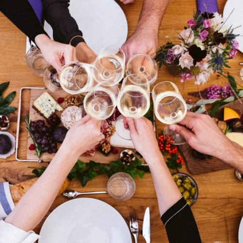 Overhead view of friends toasting with wine glasses above a table of shared food