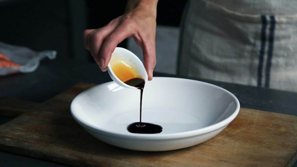 Pouring dark soy sauce from a small cup into a white bowl