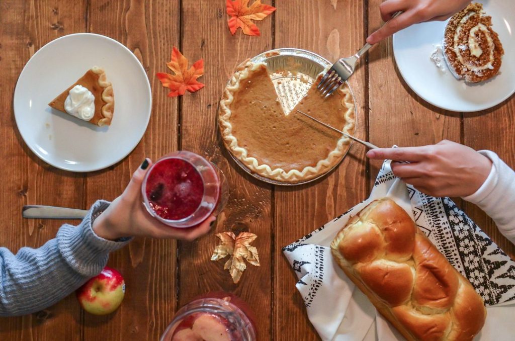 Pumpkin pie being sliced and shared on a wooden table with autumn leaves and bread