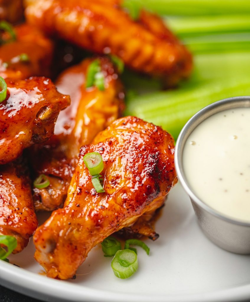 Saucy buffalo chicken drumsticks and wings with green onions, celery and ranch dip