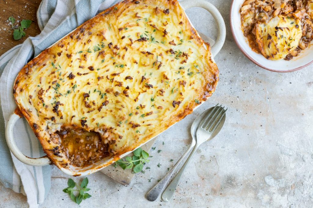 Shepherd's pie with a golden mashed potato topping in a baking dish, with a serving on a side plate