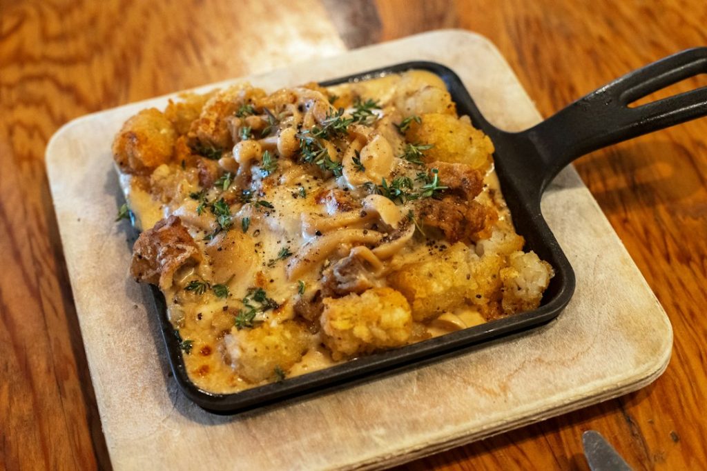 Tater tot casserole with melted cheese and caramelized onions in a cast iron skillet