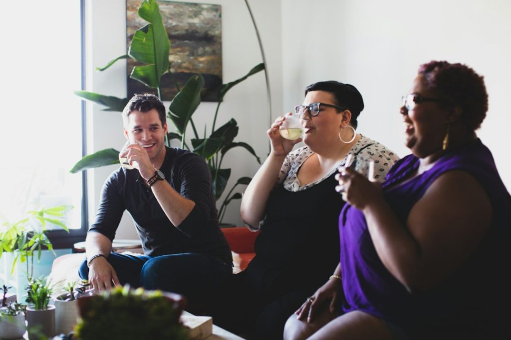Three friends sitting together in a bright room, talking and smiling with drinks