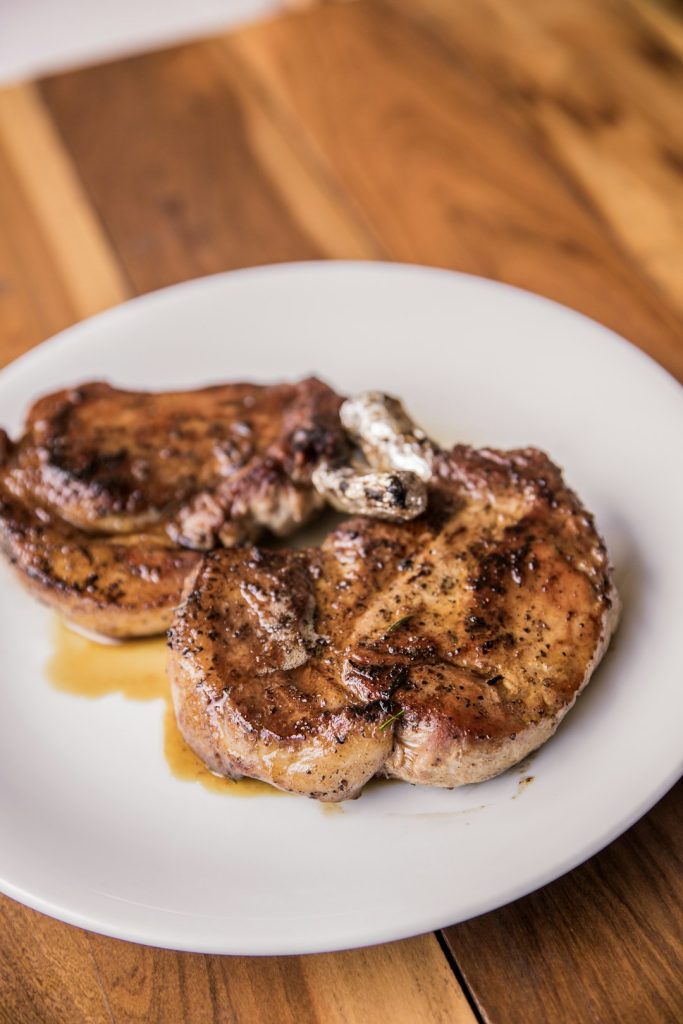 Two seared pork chops with pan sauce on a white plate